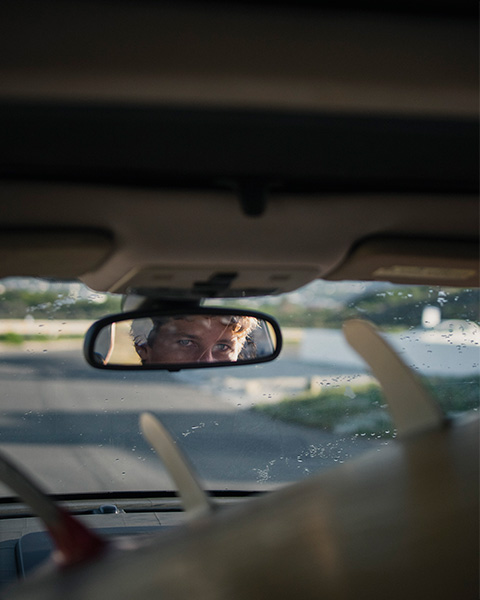 Man with blue eyes looking in the rear view mirror while driving with surfboards in the car