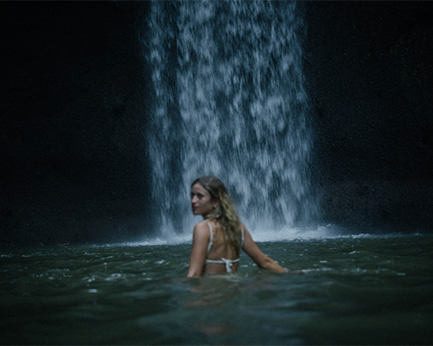 Beautiful woman walking in the water towards a big waterfall