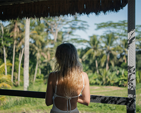Woman standing at a wooden railing at sunset with rice fields and palm trees in the background
