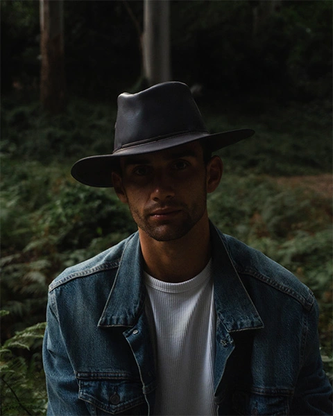 Man sitting in the woods with a denim jacket and leather hat