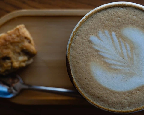 Top down shot of a coffee cup with fern foam art and a rusk and teaspoon at Spoon Eatery and Bakery