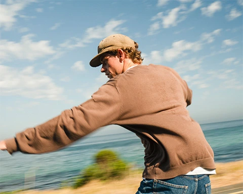 Man skateboarding on a beautiful coastal road in the morning sun with the ocean in the background